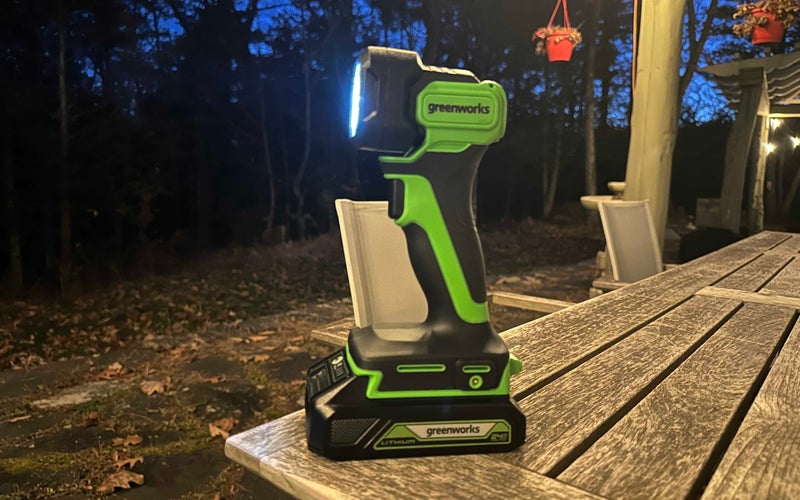 A green and black Greenworks 24V Cordless LED Flashlight outside at night on a table