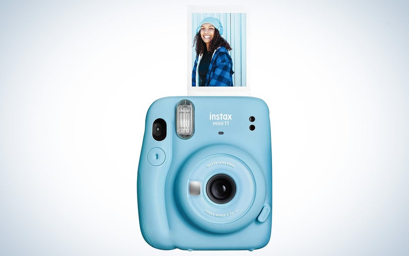 Fujifilm Instax camera with a print sticking out on a plain background